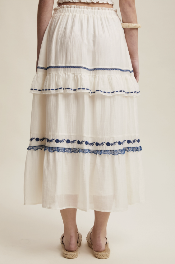 White tiered skirt with blue embroidery on a plain background