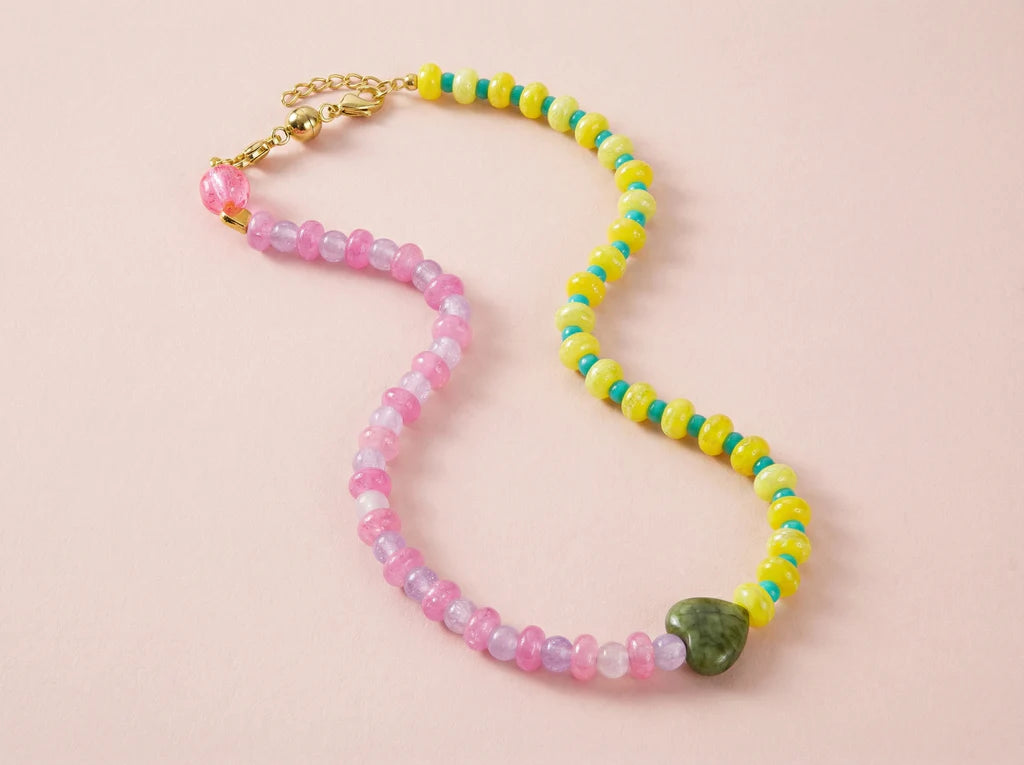 Colorful beaded necklace with a green stone on a pink background