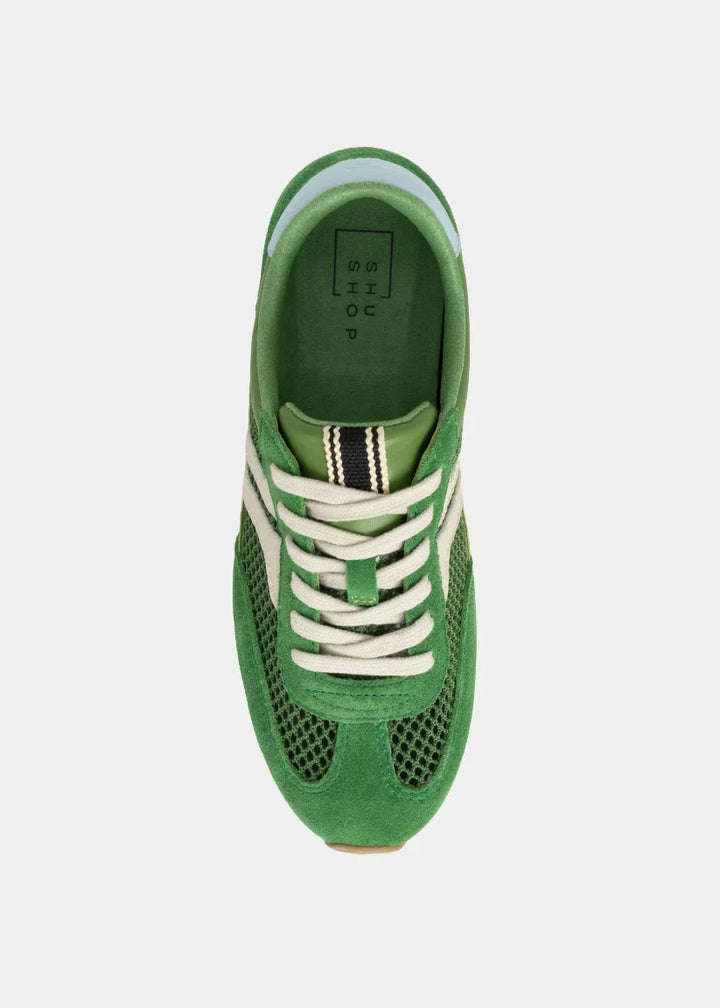 Green sneaker with white laces on a light gray background