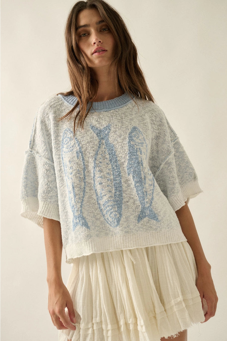 Woman wearing a light blue knit sweater with fish patterns on a plain background