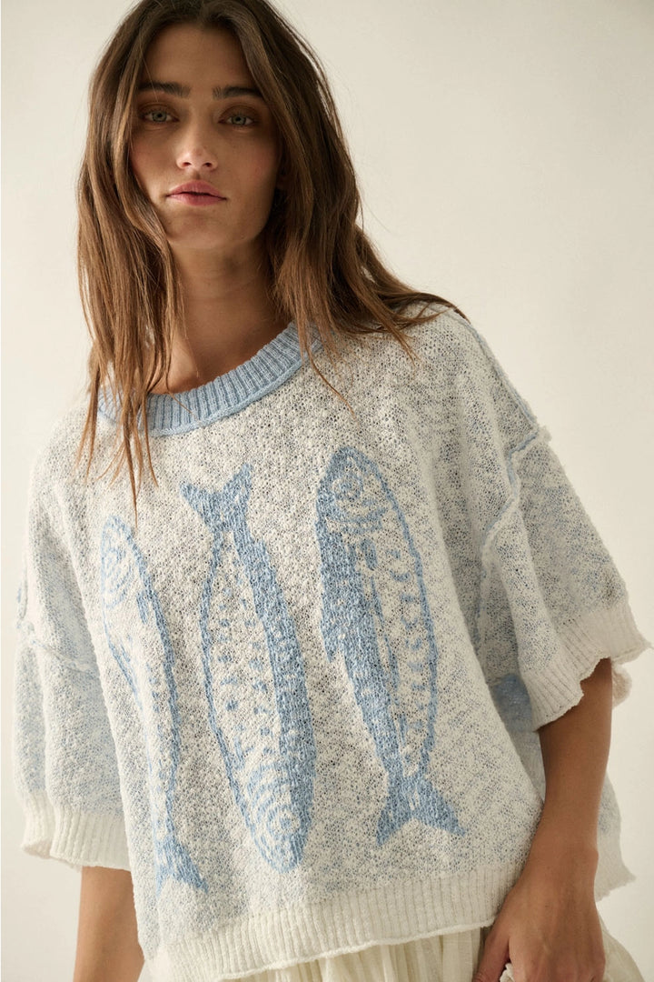 Woman wearing a light gray sweater with blue fish patterns on a plain background