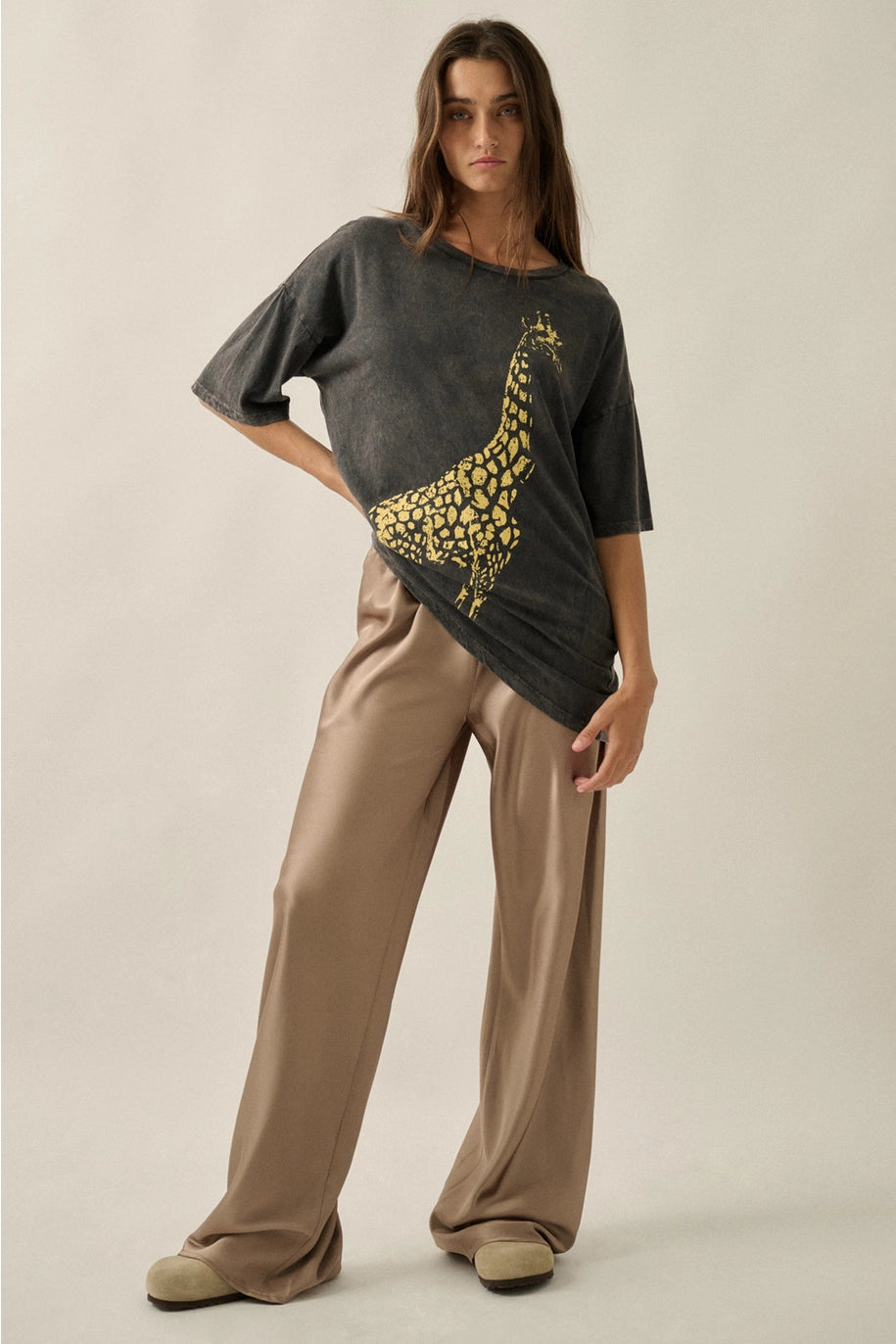 Woman wearing a dark gray t-shirt with a yellow giraffe design and beige pants on a plain background