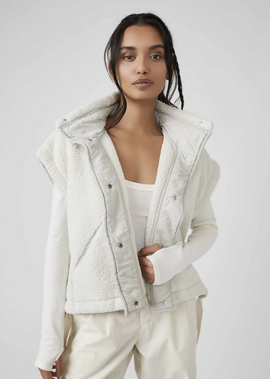 Woman wearing white fluffy vest with white long sleeve and white pants on plain background