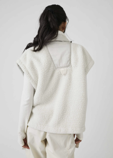 A model shown from the back wearing a textured cream sherpa fleece vest over a matching cream long-sleeve top and cream trousers, set against a plain light gray studio background.