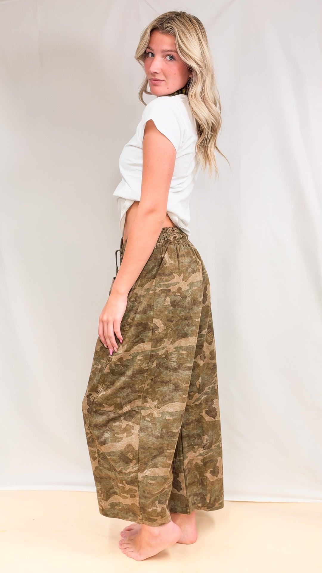 Woman wearing baby tee with camo sweatpants shown from side on plain background