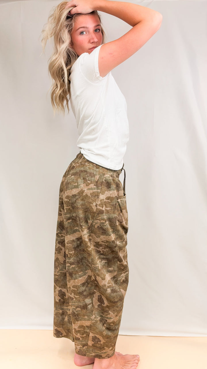 Woman wearing baby tee with camo sweatpants shown from side on plain background