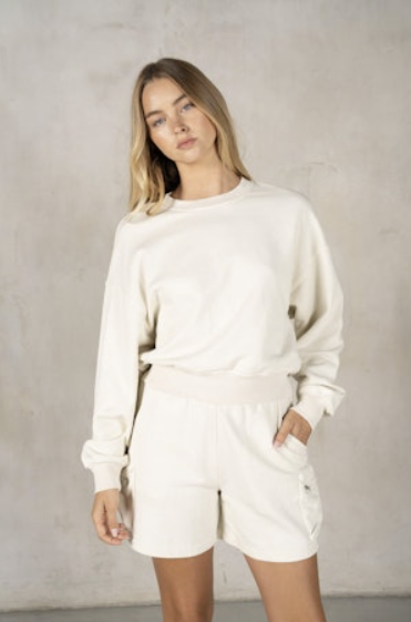 Woman wearing a white sweater and shorts set against a plain background