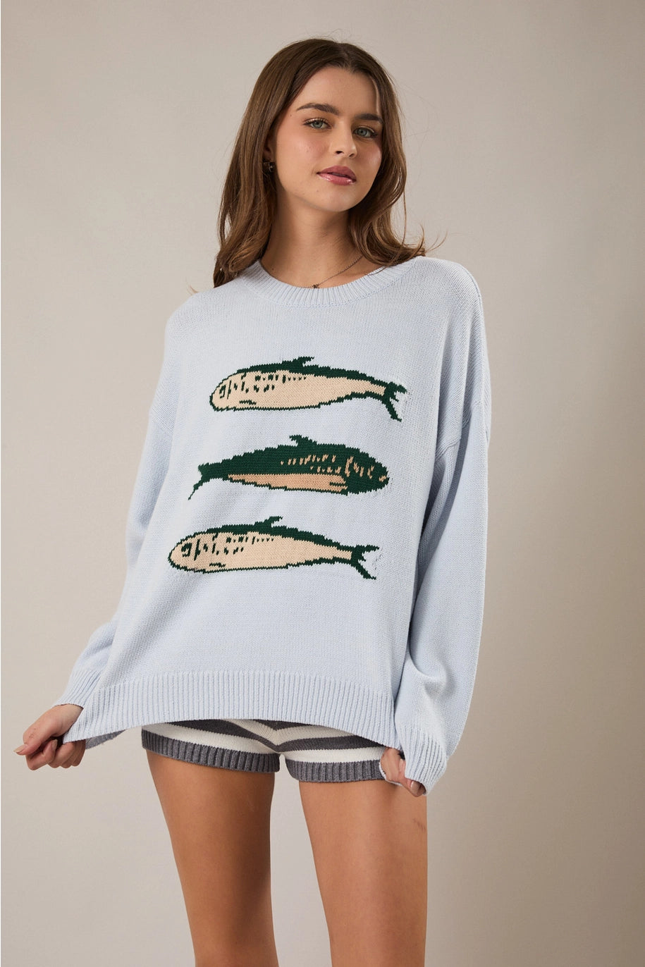 Woman wearing light blue sweater with sardine graphic on plain background
