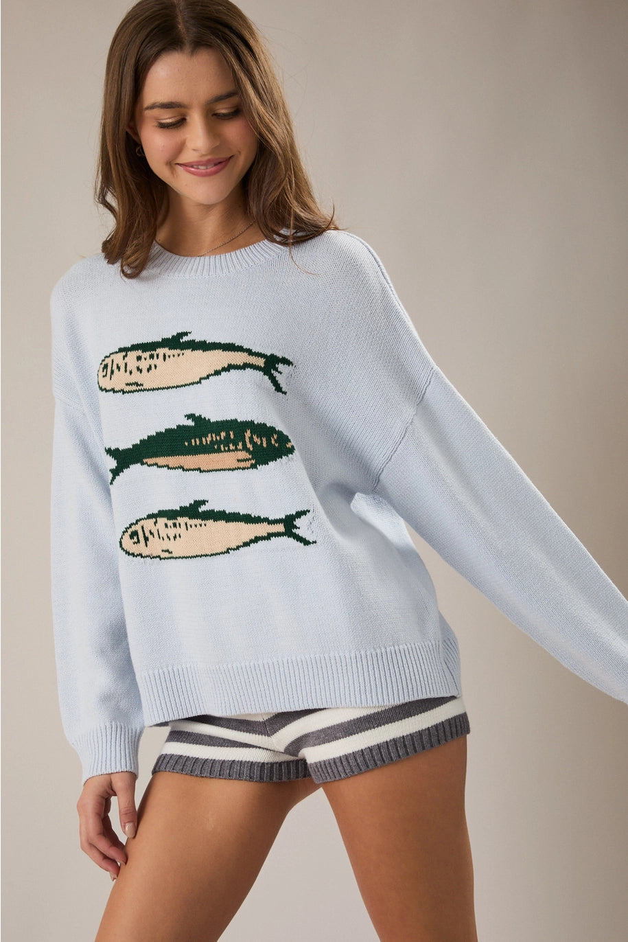 Woman wearing light blue sweater with sardine graphic on plain background
