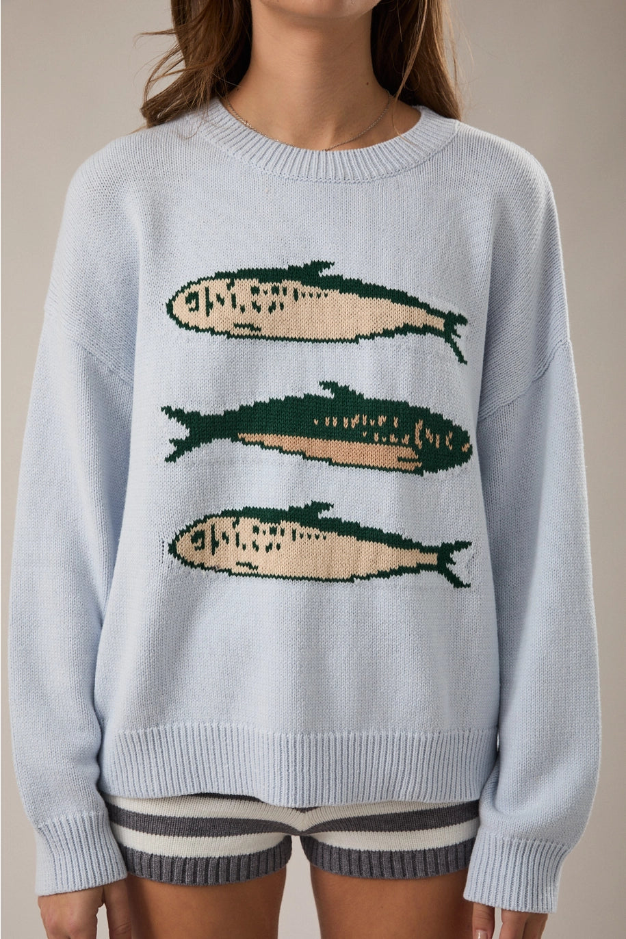 Woman wearing light blue sweater with sardine graphic on plain background