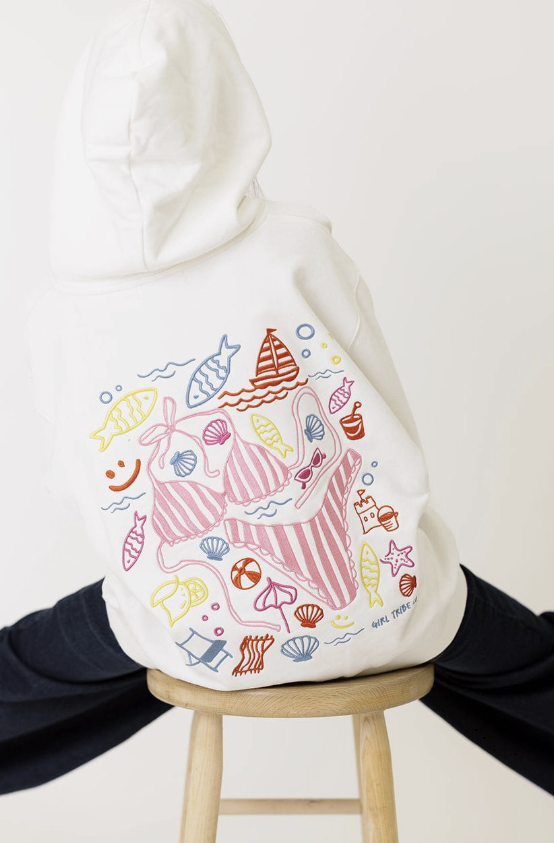 White hoodie with colorful sea-themed designs on a wooden stool