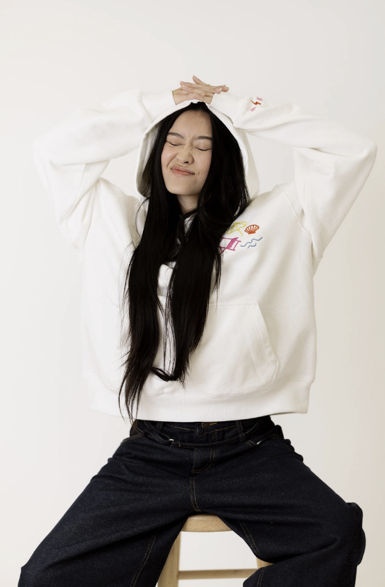 Person wearing a white hoodie with a graphic design, sitting on a stool against a plain background