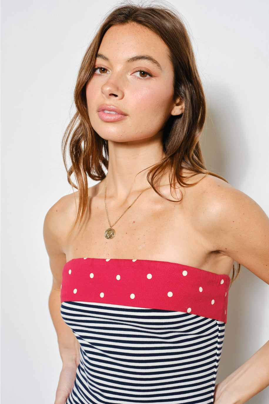 Woman wearing a strapless top with red polka dot band and black and white striped skirt against a plain background