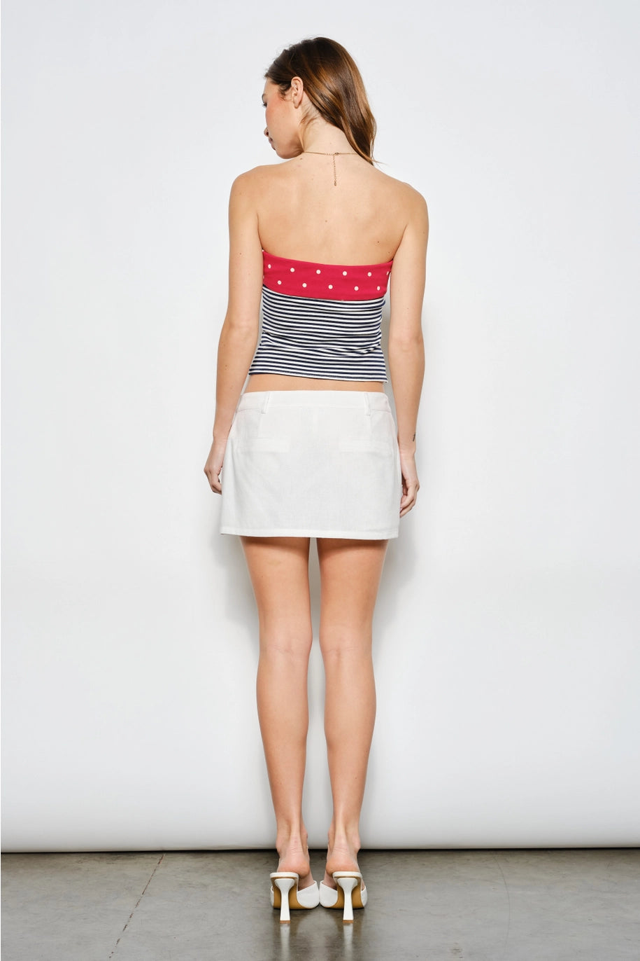 Woman wearing a striped tube top and white skirt against a plain background