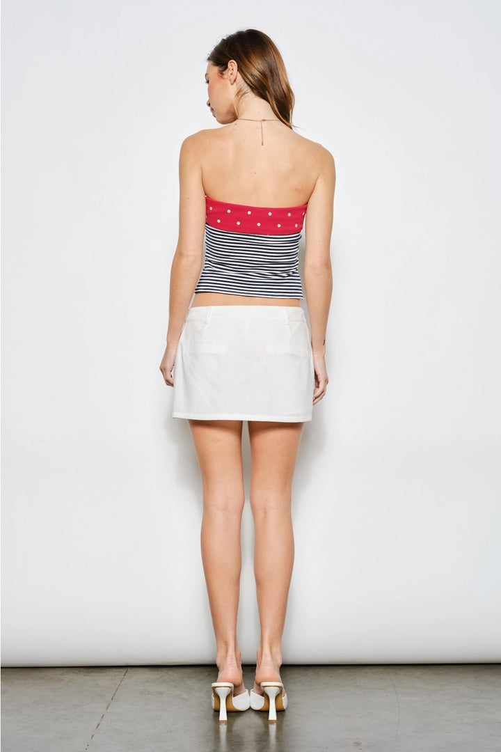 Woman wearing a striped tube top and white skirt against a plain background