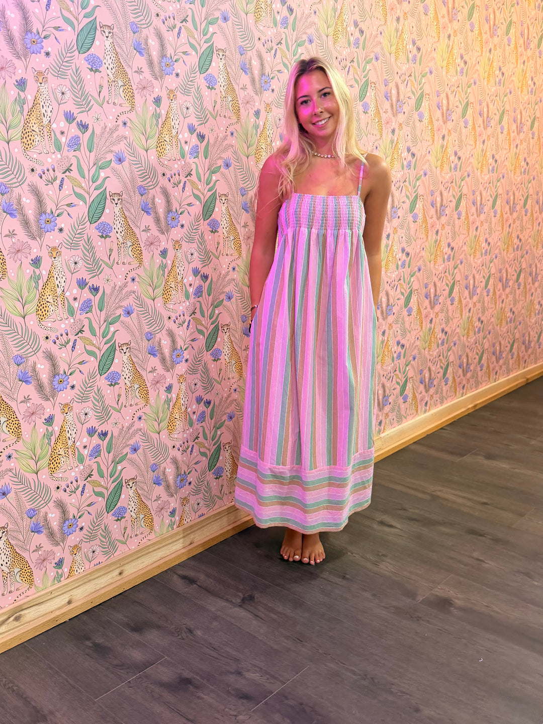 Woman in a striped dress standing against a colorful floral and animal patterned wall.