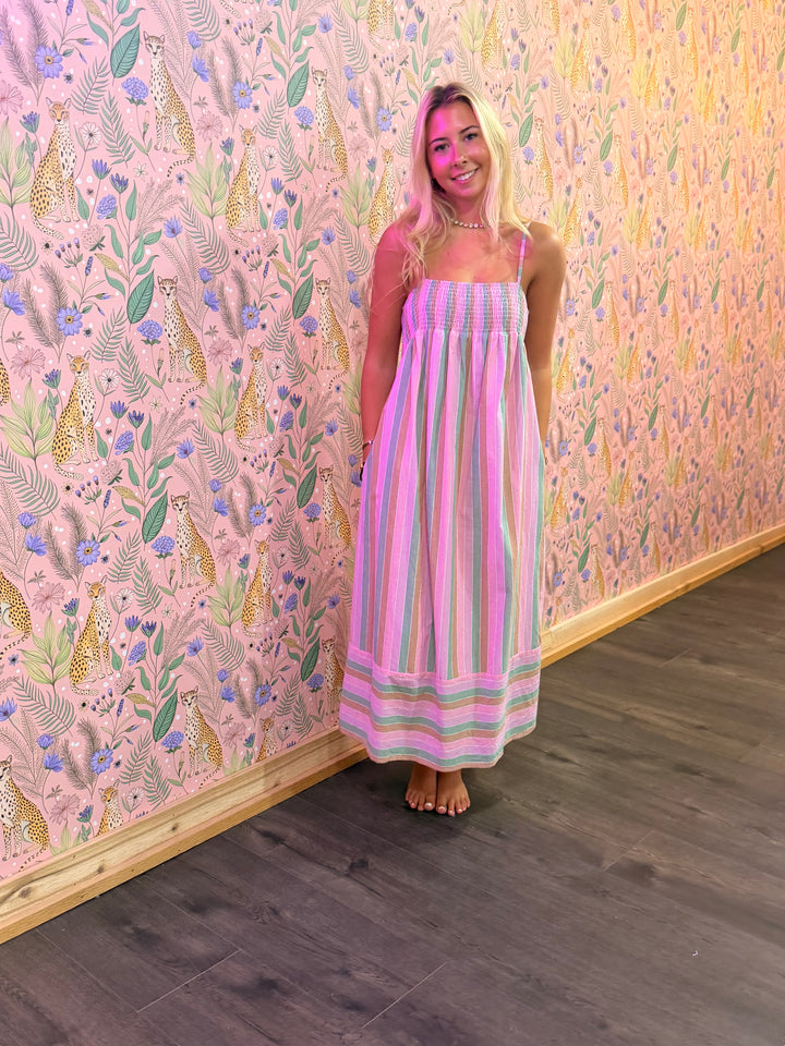 Woman in a striped dress standing against a colorful floral and animal patterned wall.