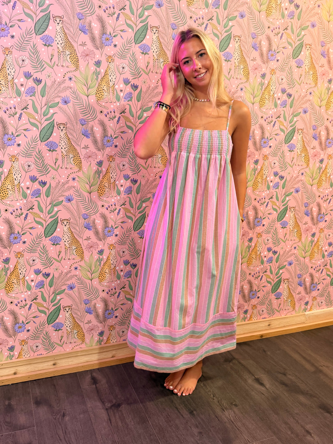 Woman in a striped dress standing against a pink wall with animal and floral pattern