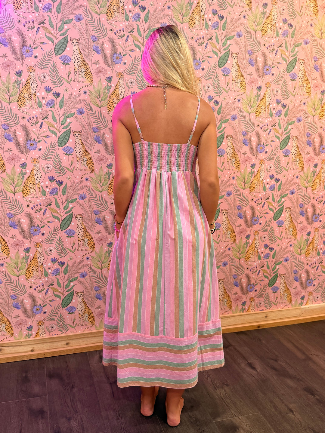 Woman in a striped dress standing in front of a pink wall with animal and floral pattern