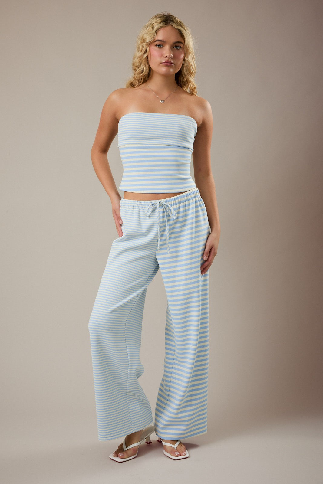 Woman wearing a light blue striped strapless top and wide-leg pants against a beige background