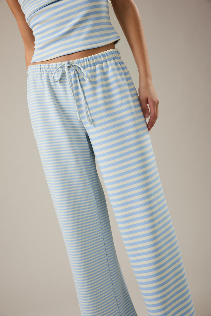 Light blue and white striped pajama pants worn by a person on a beige background
