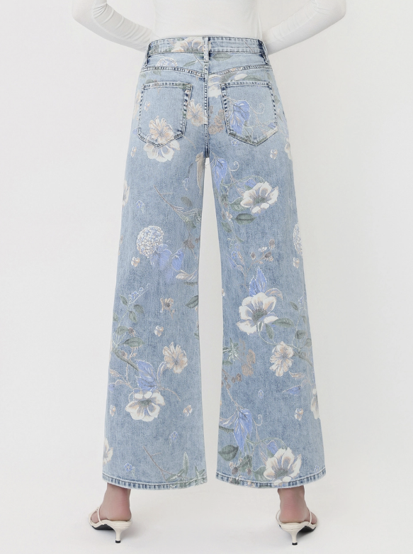 Back view of a model wearing light blue wide-leg denim jeans with an embroidered floral pattern, paired with white high-heeled sandals against a plain white background.