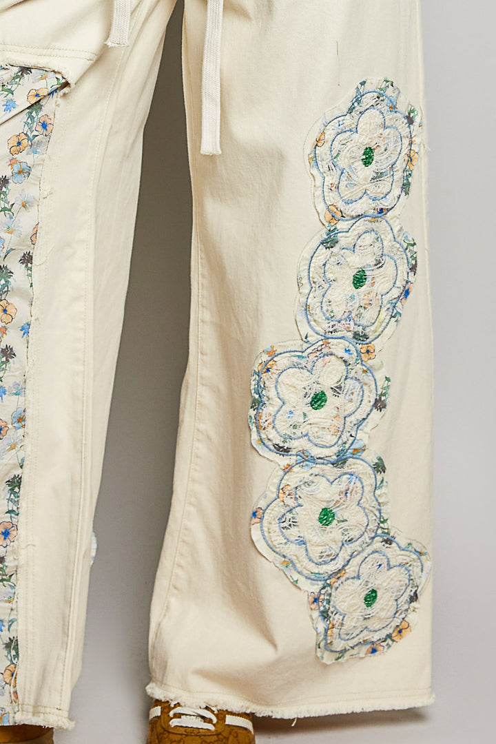 Beige pants with floral embroidery on a plain background