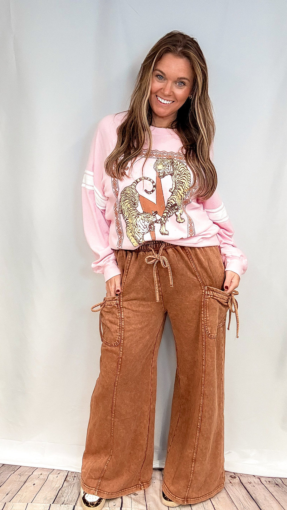 Woman wearing brown lounge pants with pink graphic sweatshirt on white background
