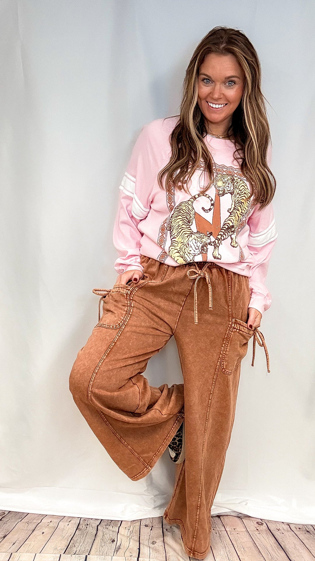 Woman wearing brown lounge pants with pink graphic sweatshirt on white background