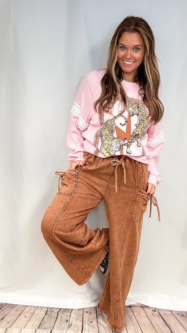Woman wearing brown lounge pants with pink graphic sweatshirt on white background