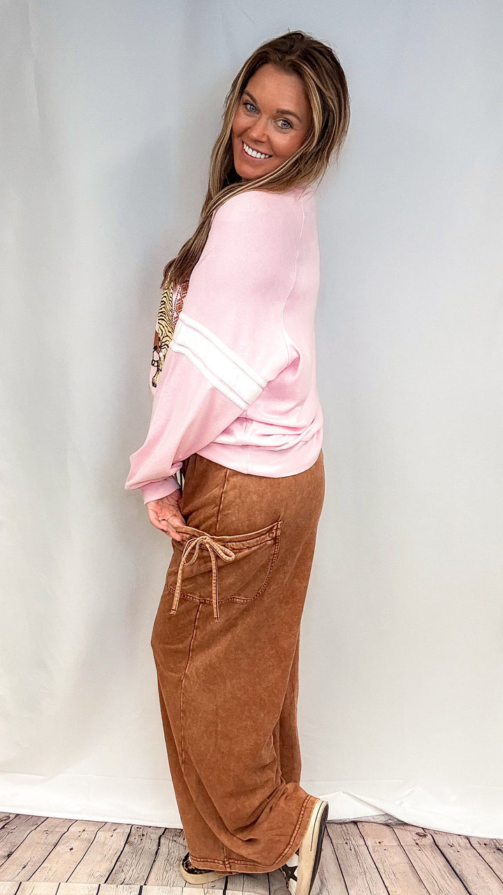 Woman wearing brown lounge pants with pink graphic sweatshirt on white background