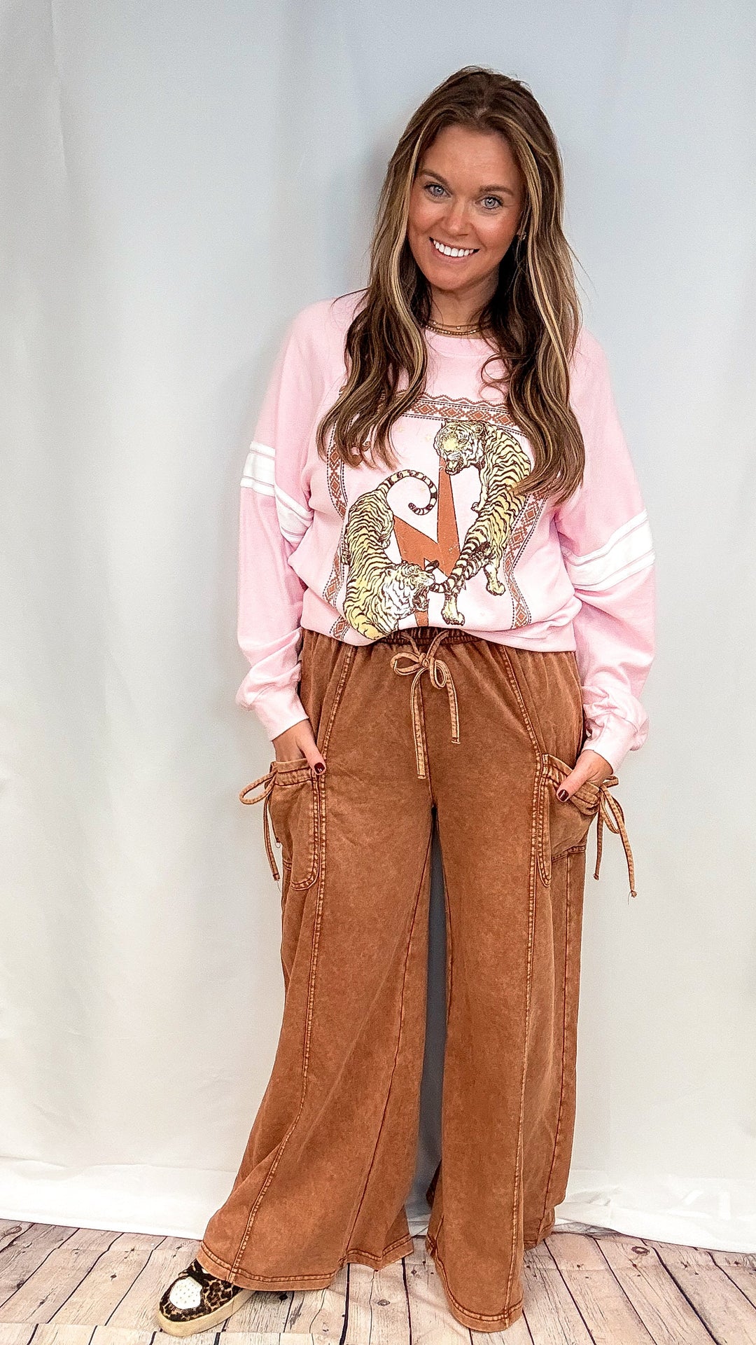 Woman wearing brown lounge pants and pink graphic sweatshirt on white background