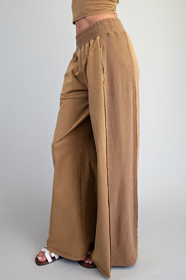 A person shown from the waist down wearing wide-leg tan pants with side slits and white slide sandals, photographed against a plain light gray studio background.