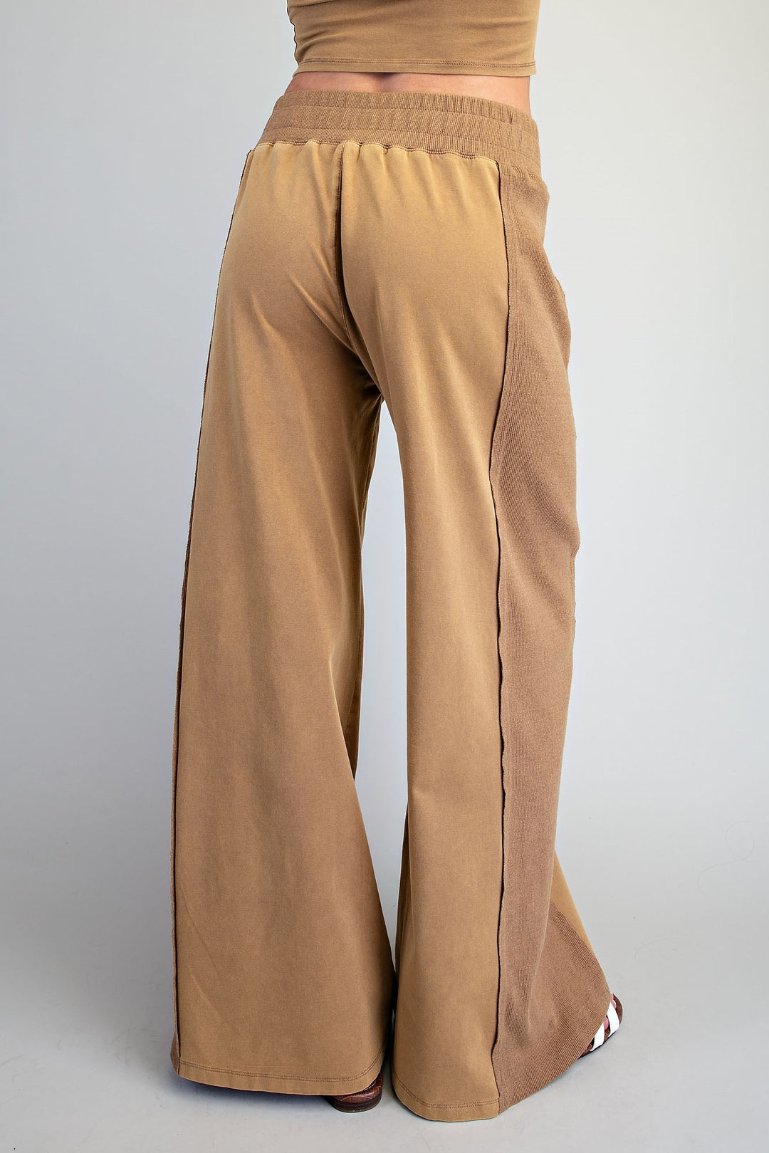 A person shown from the back wearing tan wide-leg pants with an elastic waistband, photographed against a light gray studio background.