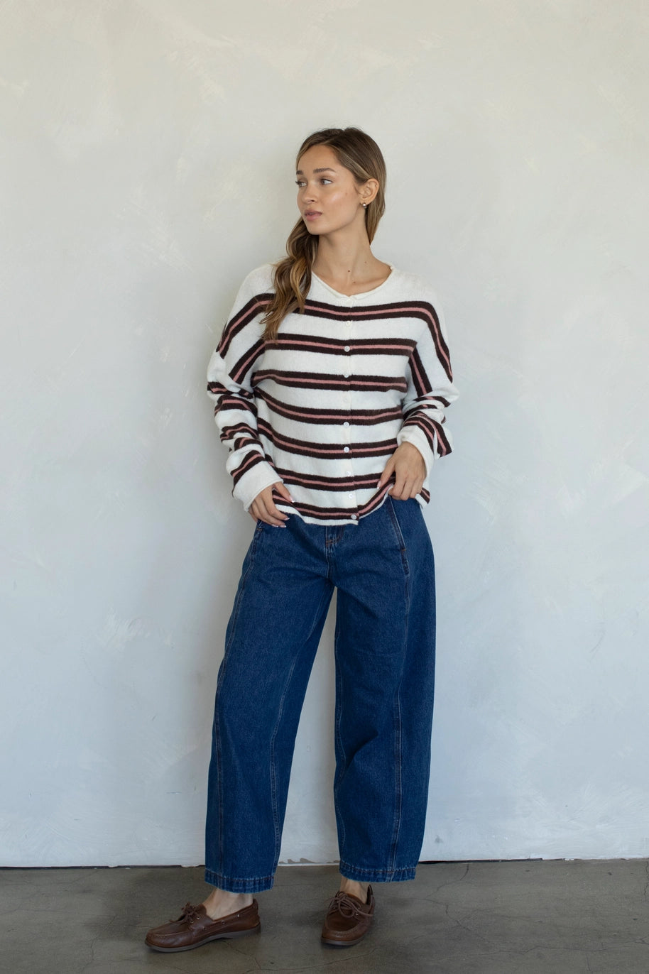 Woman wearing a striped sweater and blue jeans against a white wall
