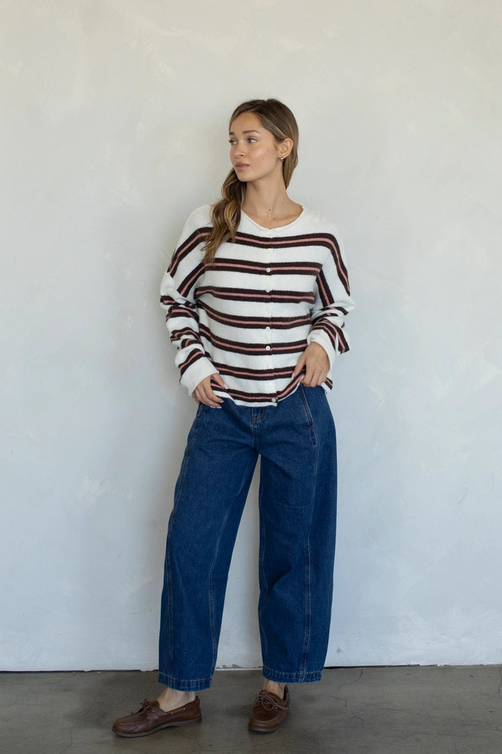 Woman wearing a striped sweater and blue jeans against a white wall