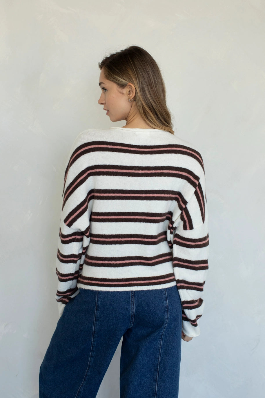 Person wearing a striped sweater and blue jeans against a white wall