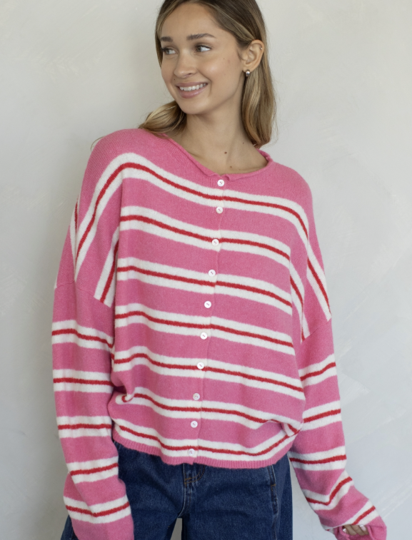 Woman wearing pink, red and white stripe cardigan and jeans on plain background