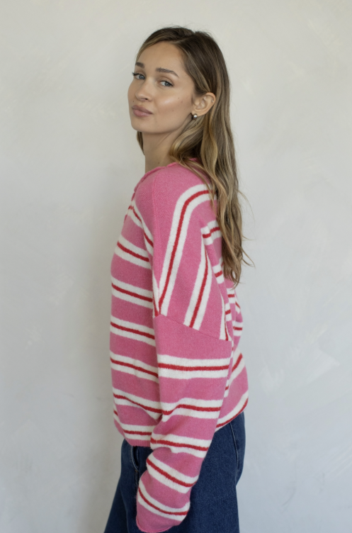 Woman wearing pink, red and white stripe cardigan and jeans on plain background