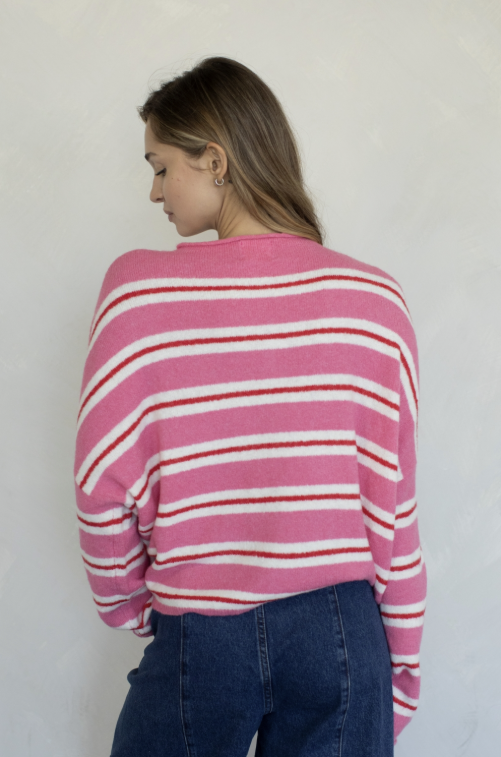 Woman shown from behind wearing pink, red and white stripe cardigan and jeans on plain background