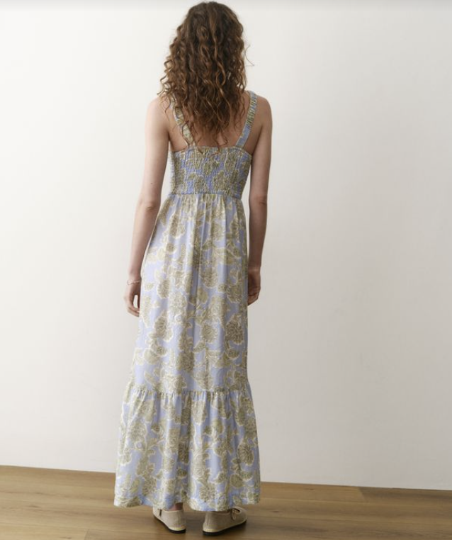 Woman wearing a patterned dress standing against a white wall.