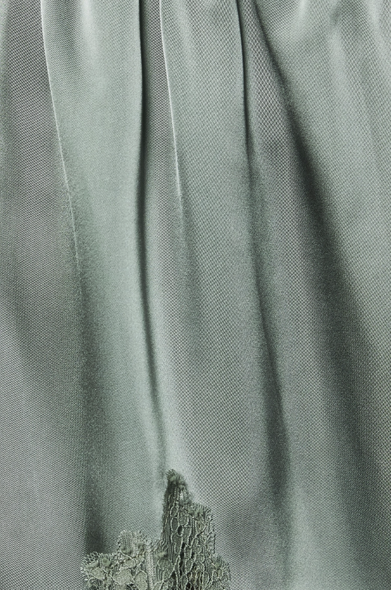 A close-up of draped sage green fabric with a textured, embroidered or lace-like embellishment near the bottom center.