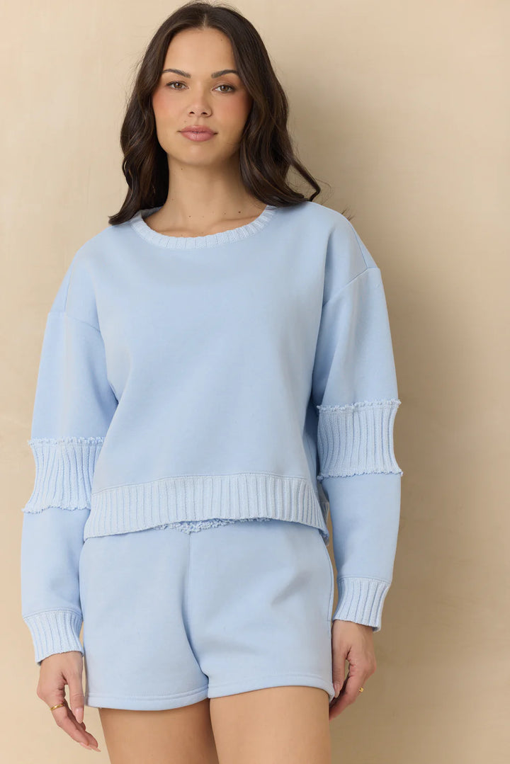 Woman wearing a light blue sweater and shorts set against a beige background