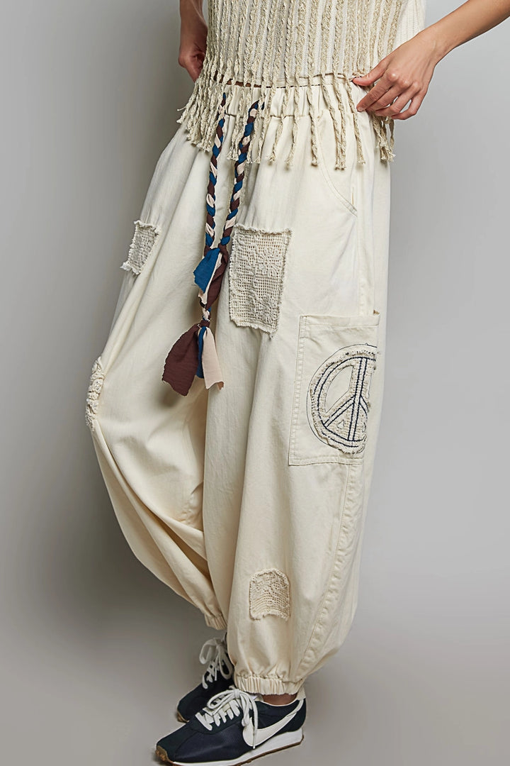 Beige baggy pants with a peace symbol patch worn by a person on a plain background
