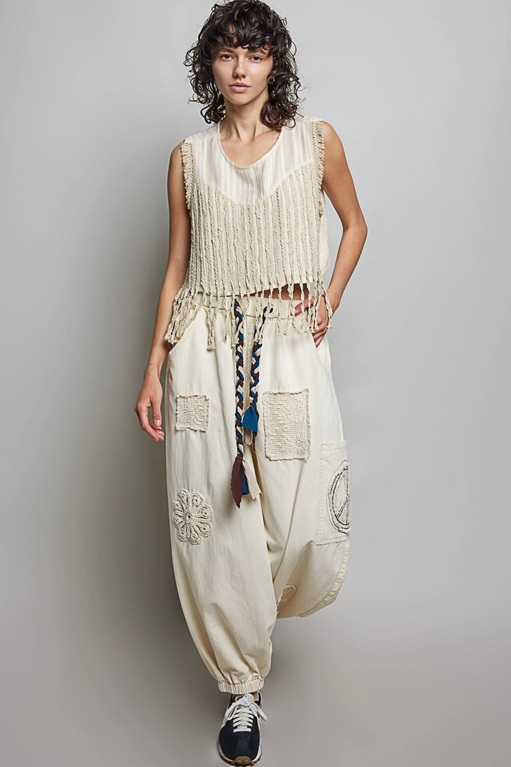 Woman wearing a sleeveless top and patchwork pants against a plain background
