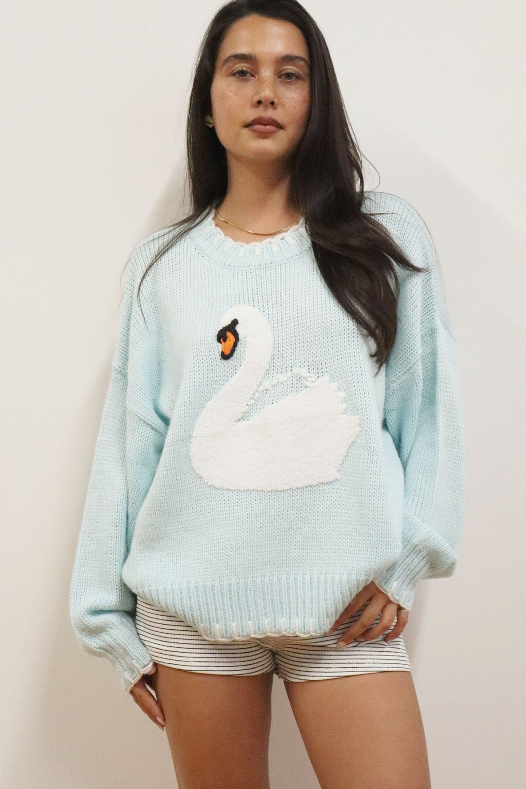 Woman wearing a light blue sweater with a swan design against a plain background