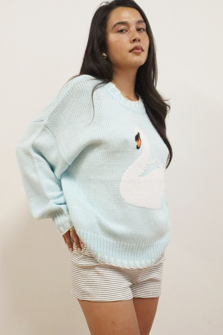 Woman wearing a light blue sweater with a white cloud design on a plain background