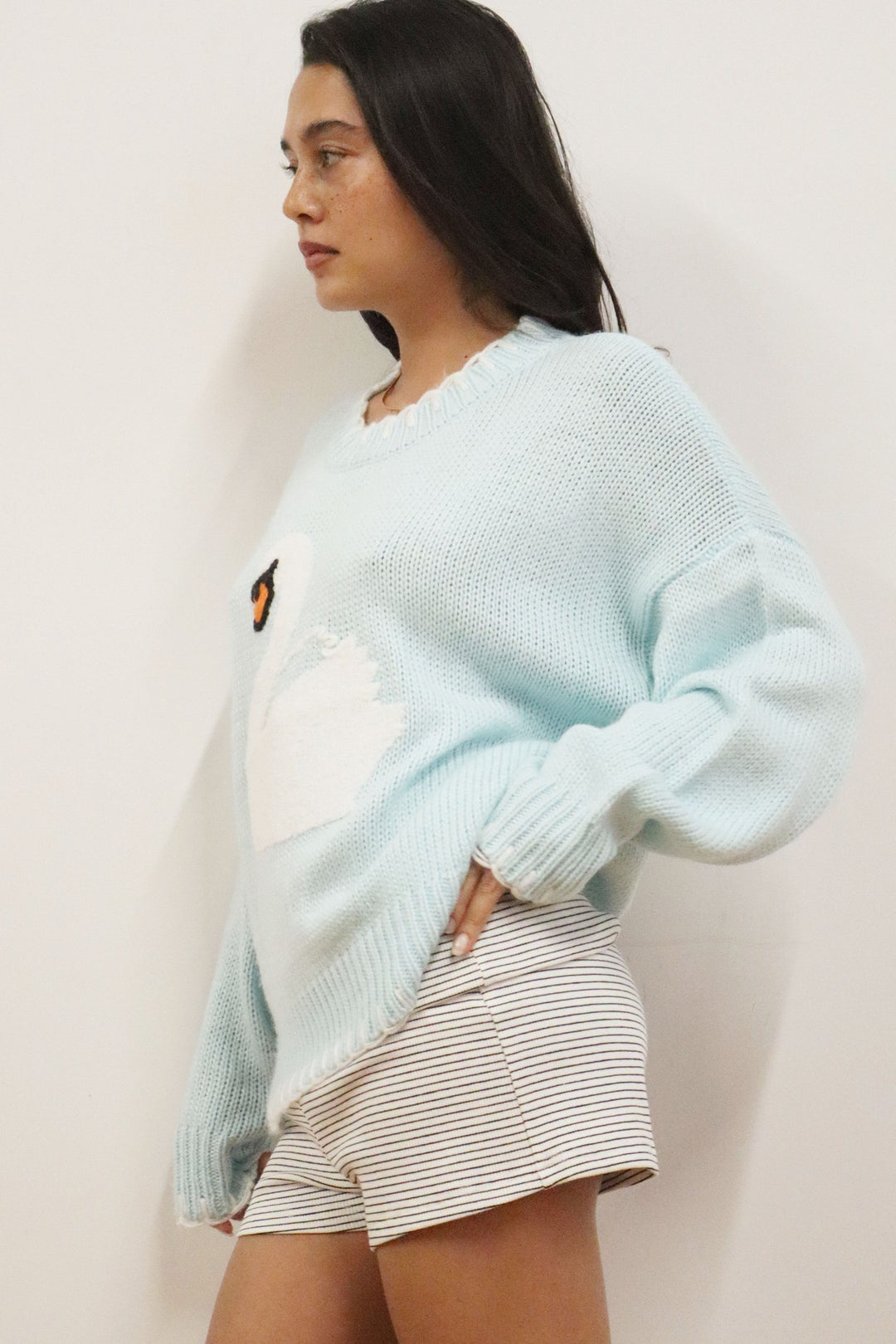 Woman wearing a light blue sweater and striped shorts against a plain background
