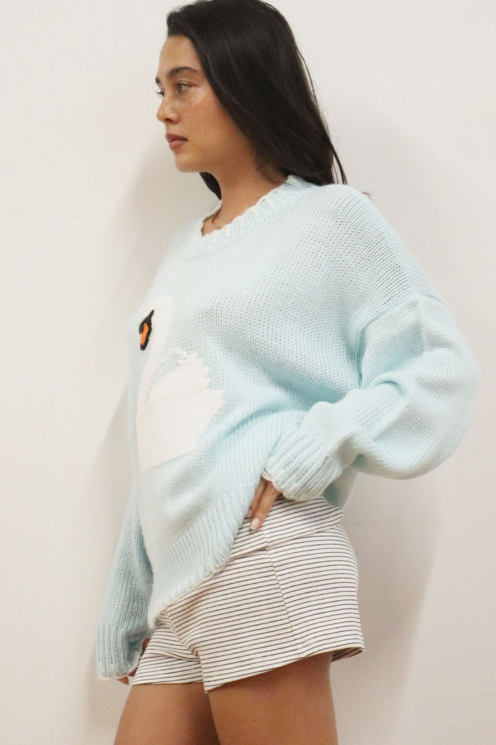 Woman wearing a light blue sweater and striped shorts against a plain background