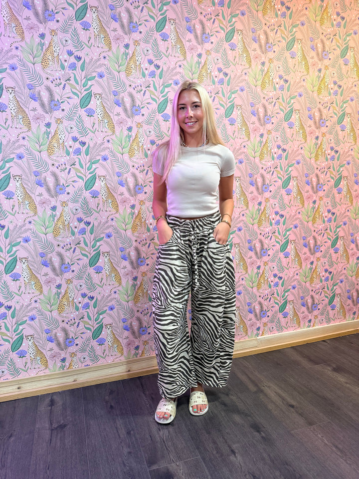 Woman wearing zebra print sweats and beige top in front of floral background